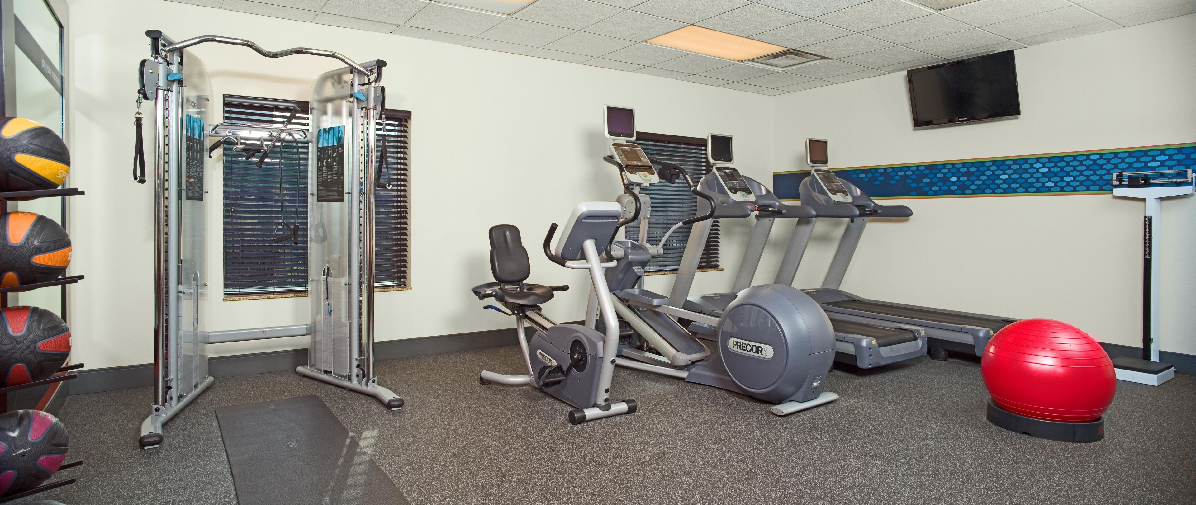 Ein Fitnessraum mit Trainingsgeräten, darunter Laufband, Crosstrainer und Gewichte.