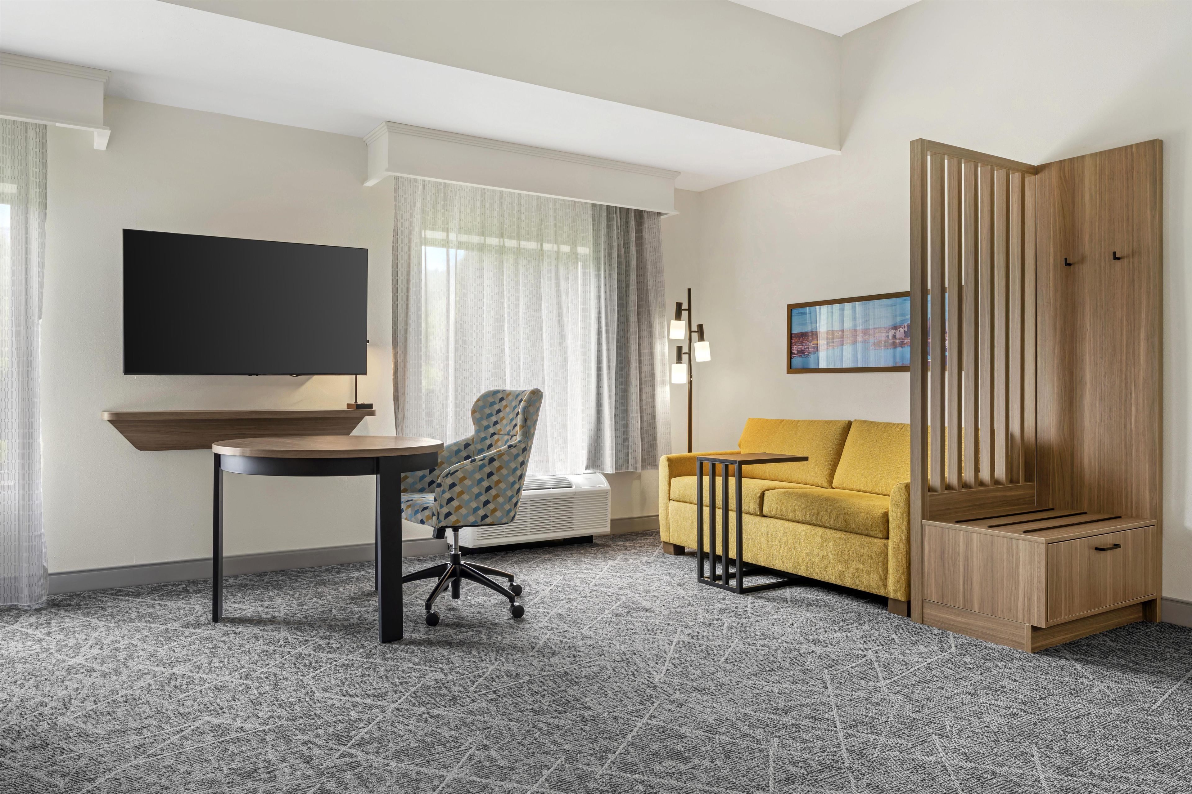 A hotel room with a flat-screen TV, a sofa, a chair, a small table, and a wooden wardrobe.