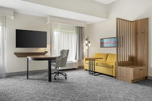 A hotel room with a flat-screen TV, a sofa, a chair, a small table, and a wooden wardrobe.