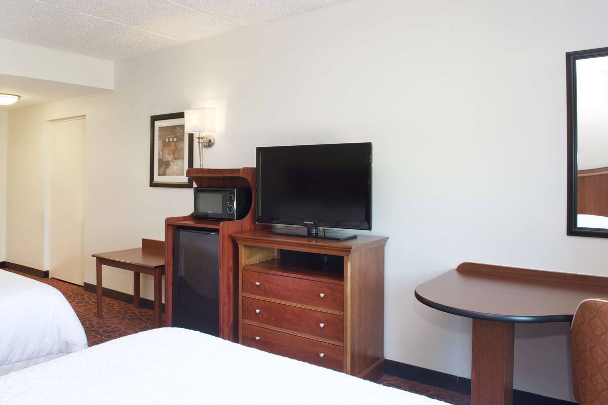 Une chambre d’hôtel avec deux lits, un bureau avec une télévision, un micro-ondes et une petite table.