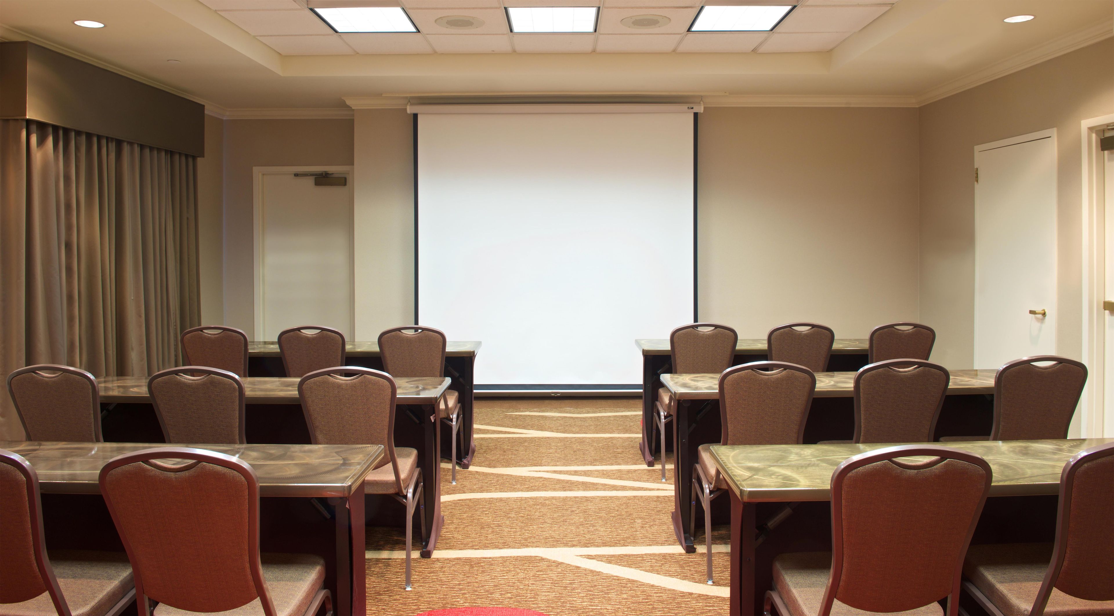 Une salle de conférence dotée d’un grand écran de projection, de plusieurs tables et de chaises disposées pour les réunions.