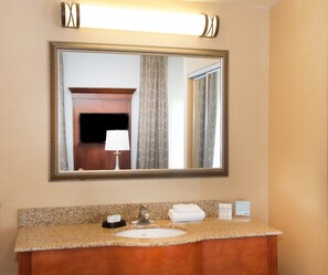 A bathroom with a granite countertop, a sink, a mirror, a towel rack, and a wall-mounted light fixture. - Hampton Inn & Suites Pittsburgh-Meadow Lands (Washington)