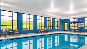 A swimming pool with clear blue water, surrounded by large windows offering views of a green landscape. There are lounge chairs and a table near the pool. - Hampton Inn & Suites Hopkinsville (Hopkinsville)