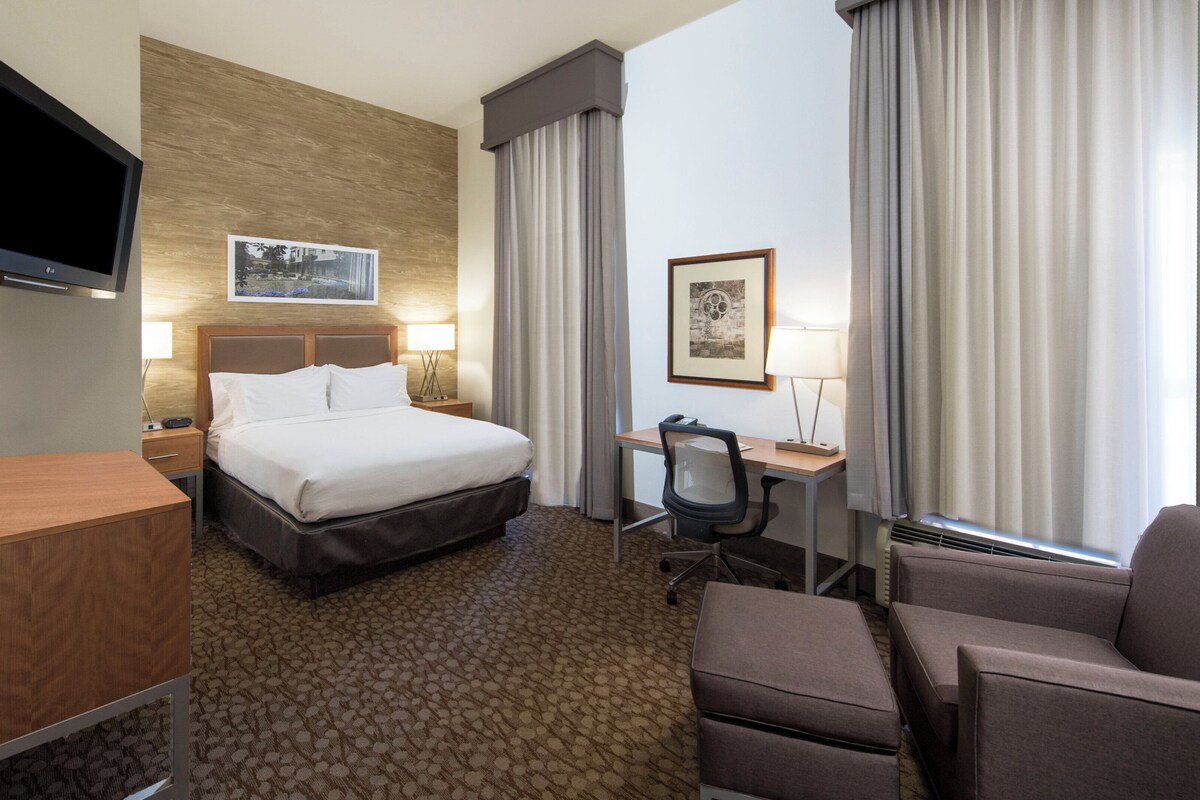 A hotel room with a bed, desk, chair, TV, and artwork on the walls.