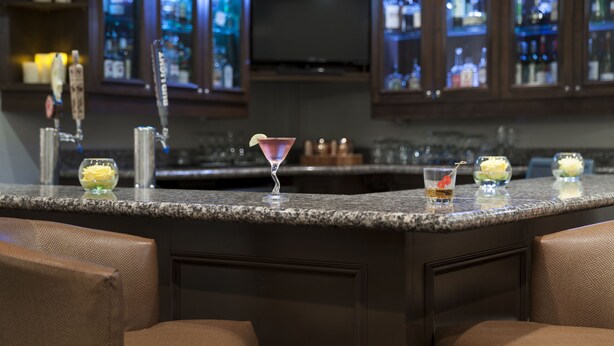 Eine Barbereich mit Granitarbeitsplatten, Barhocker und einer gefüllten Minibar mit Flaschen.