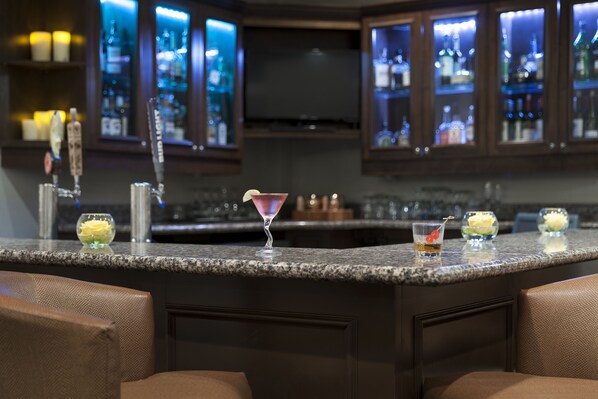 A bar area with granite countertops, bar stools, and a minibar stocked with bottles. - Holiday Inn Savannah Historic District by IHG (Savannah)
