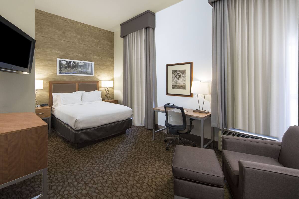 A hotel room with a bed, desk, chair, TV, and artwork on the walls.