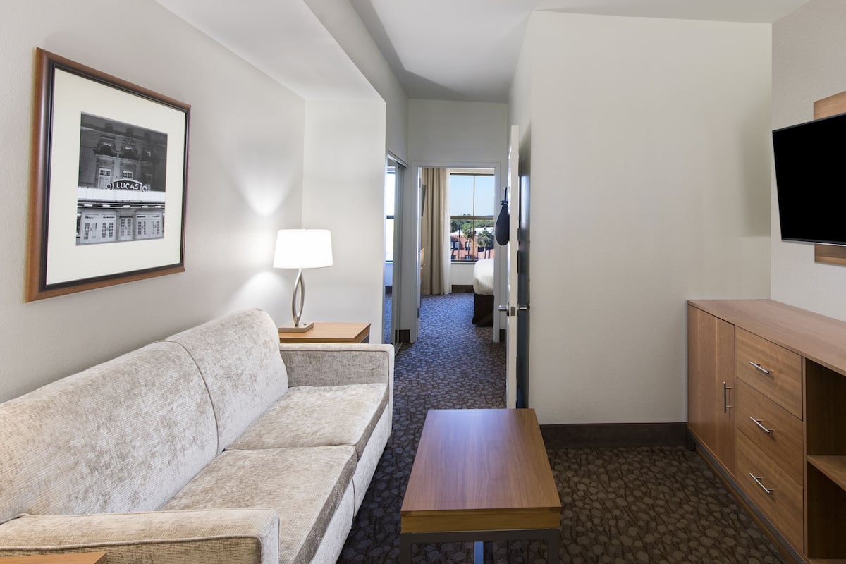 A hotel room with a sofa, a wooden cabinet, a flat-screen TV, a framed picture, and a lamp.