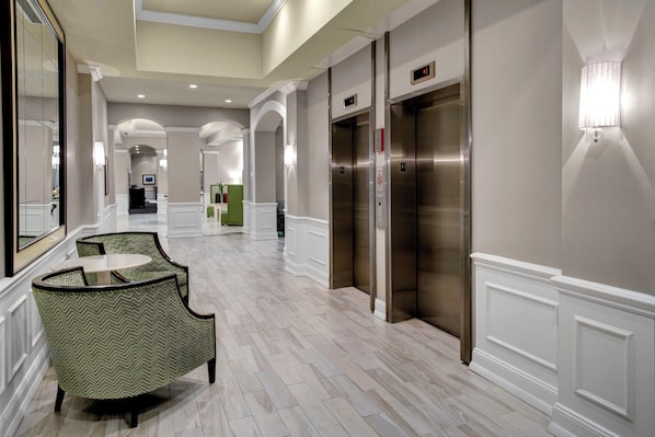 Un vestíbulo de hotel con piso de mármol, una recepción y dos ascensores.