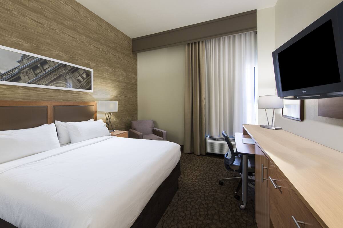 A hotel room with a large bed, a desk with a TV, a chair, and a window with curtains.