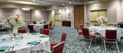 A hotel conference room with round tables, red chairs, and white tablecloths.