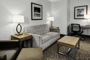 A modern hotel room with a grey sofa, a wooden coffee table, a desk, and two lamps. - Holiday Inn Savannah Historic District by IHG (Savannah)