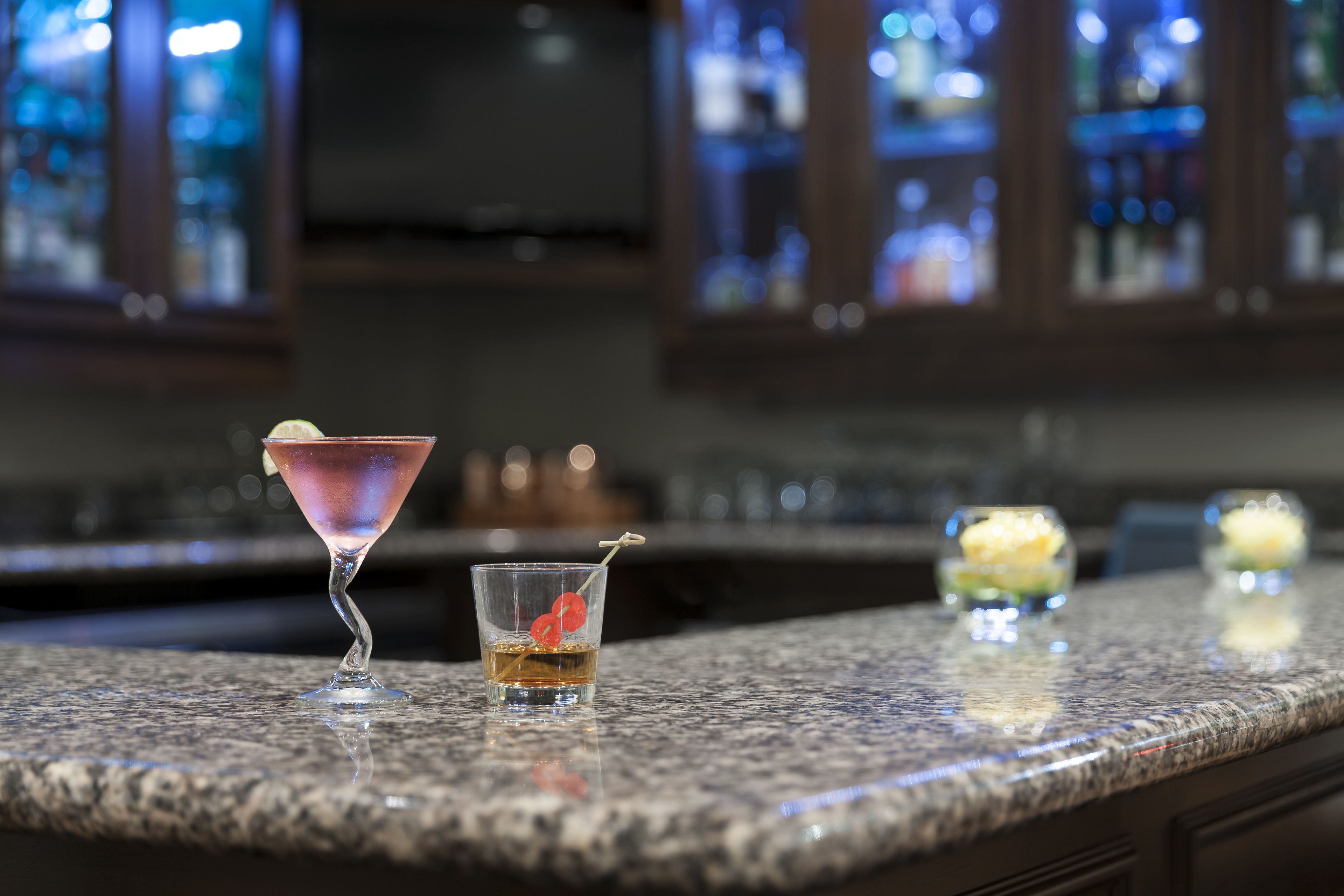 A bar counter with three drinks: a martini, a whiskey, and a cocktail with a lime garnish.