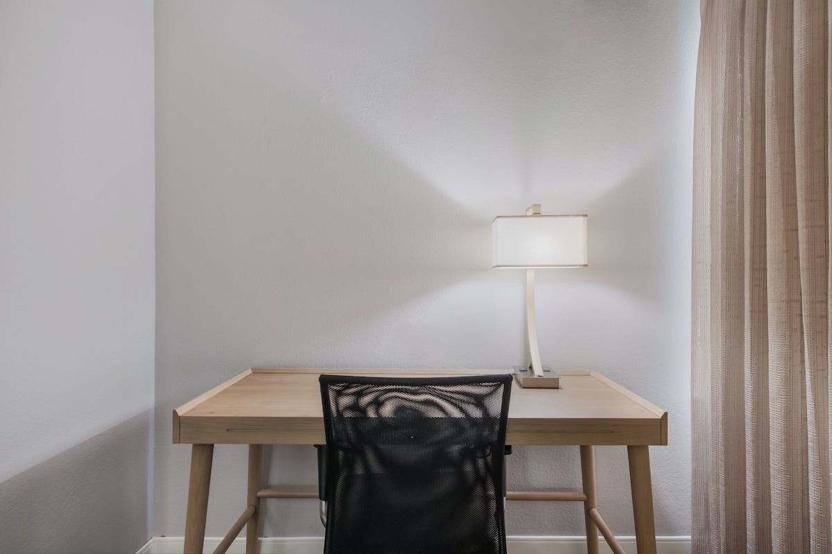 A small, simple desk with a chair and a lamp in a corner of a room.