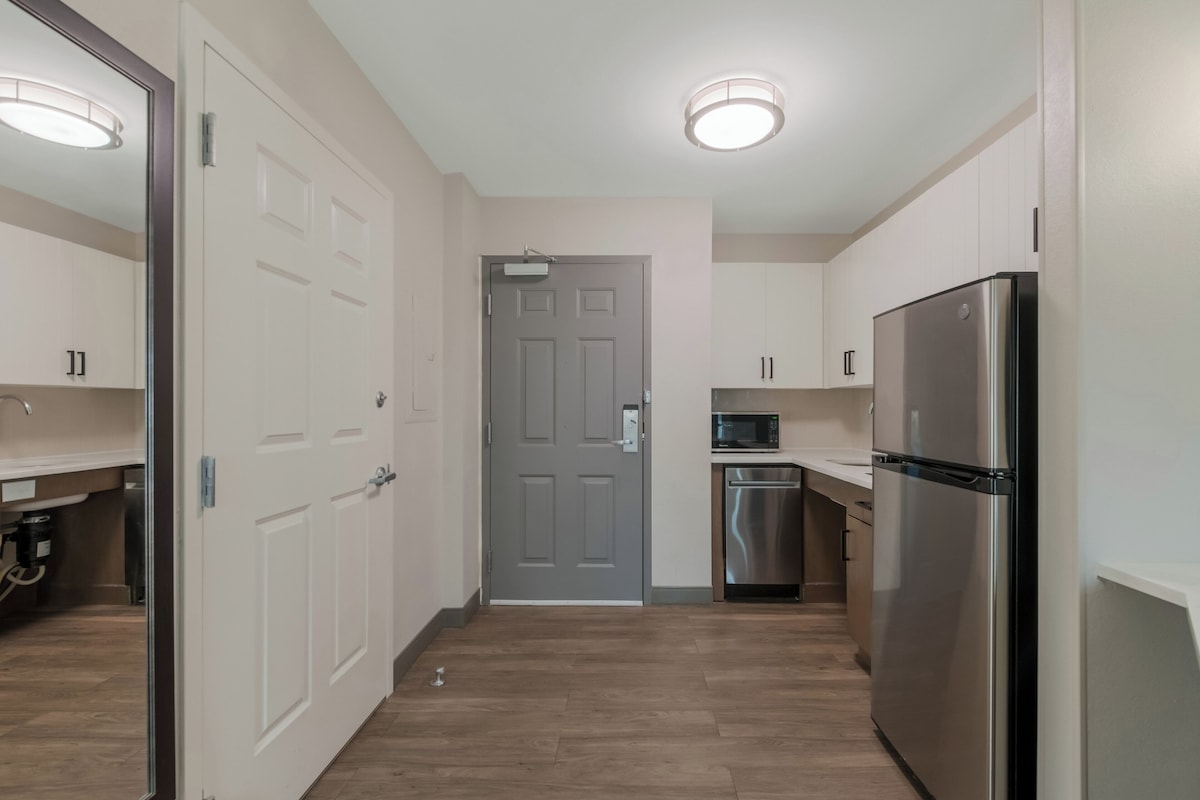 A modern kitchen with white cabinets, a stainless steel refrigerator, a microwave, and a dishwasher.