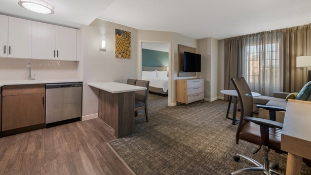 A hotel room with a kitchenette, a dining area, a bed, a TV, and a window with curtains. - Staybridge Suites Chesapeake by IHG (Chesapeake)
