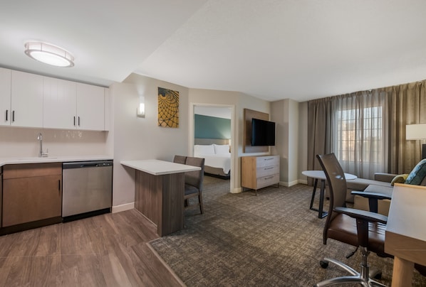 A hotel room with a kitchenette, a dining area, a bed, a TV, and a window with curtains. - Staybridge Suites Chesapeake by IHG (Chesapeake)