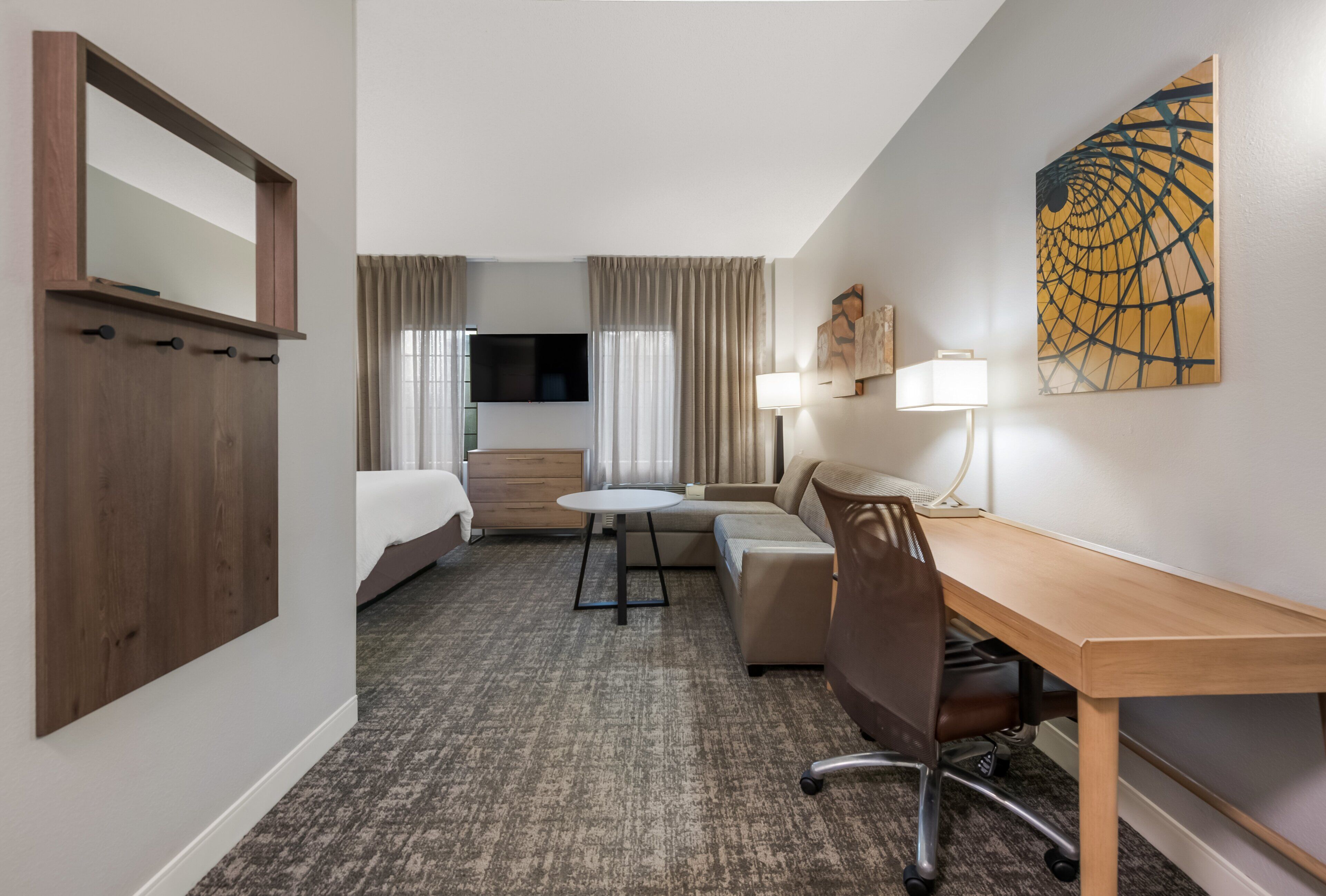 A hotel room with a bed, a desk, a chair, a TV, and a painting on the wall.