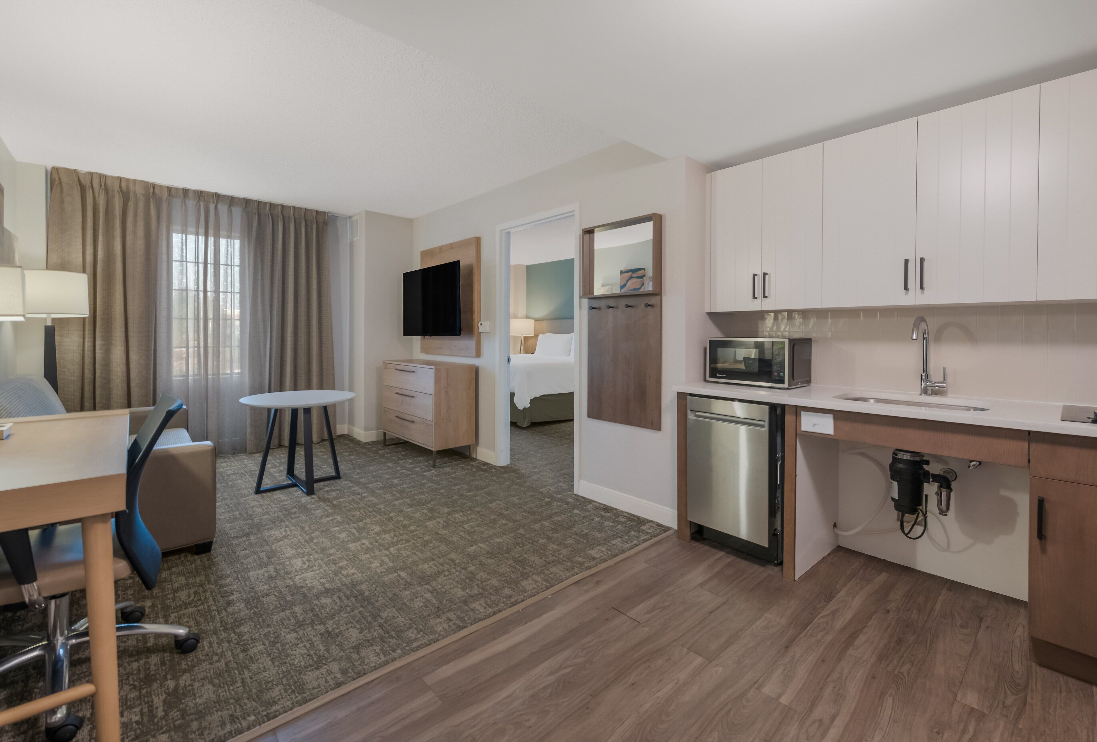 A hotel room with a kitchenette, a dining area, a TV, and a bed.