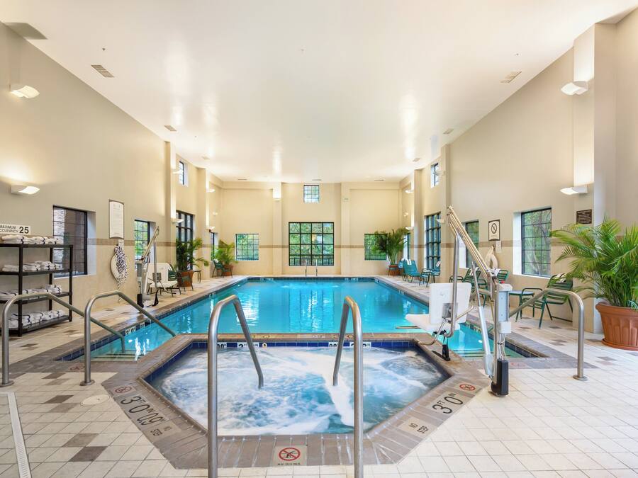 An indoor swimming pool with a hot tub, surrounded by lounge chairs and potted plants.