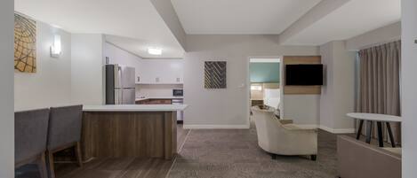 Habitación de hotel moderna con kitchenette, zona de estar con sofá y sillones, televisión de pantalla plana y alfombra estampada.