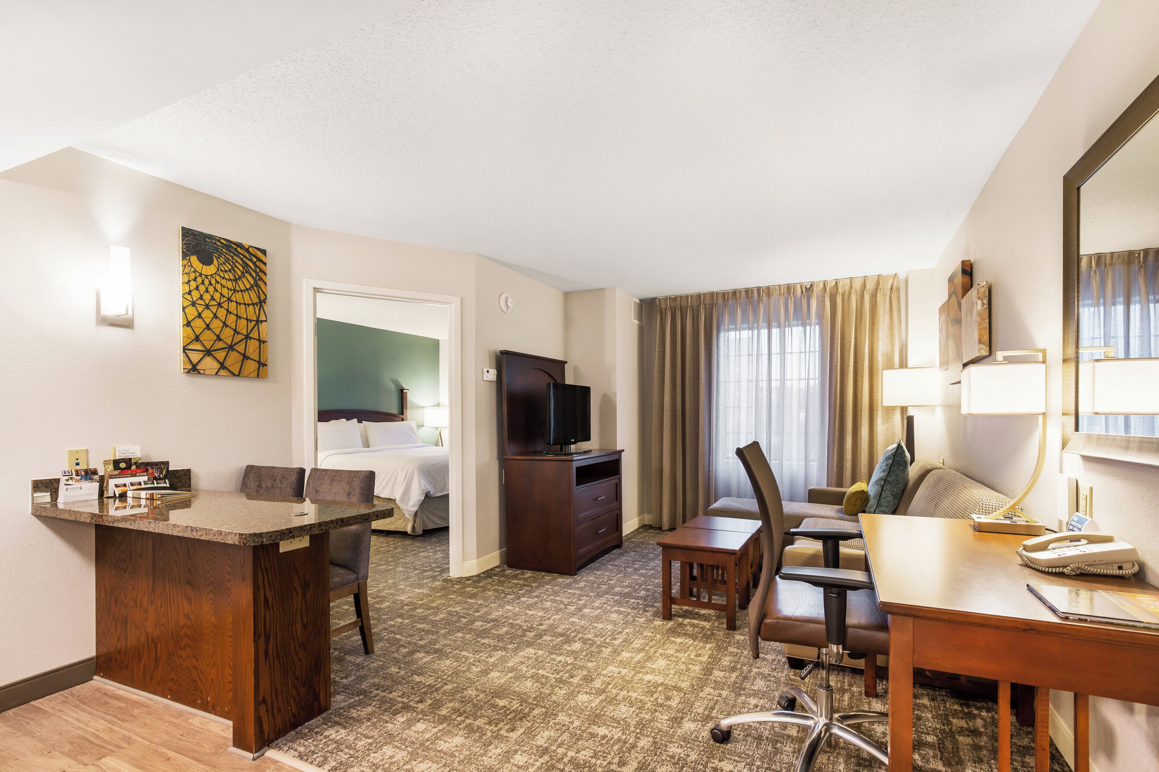 A hotel room with a bed, a desk, a chair, a television, and a desk lamp.