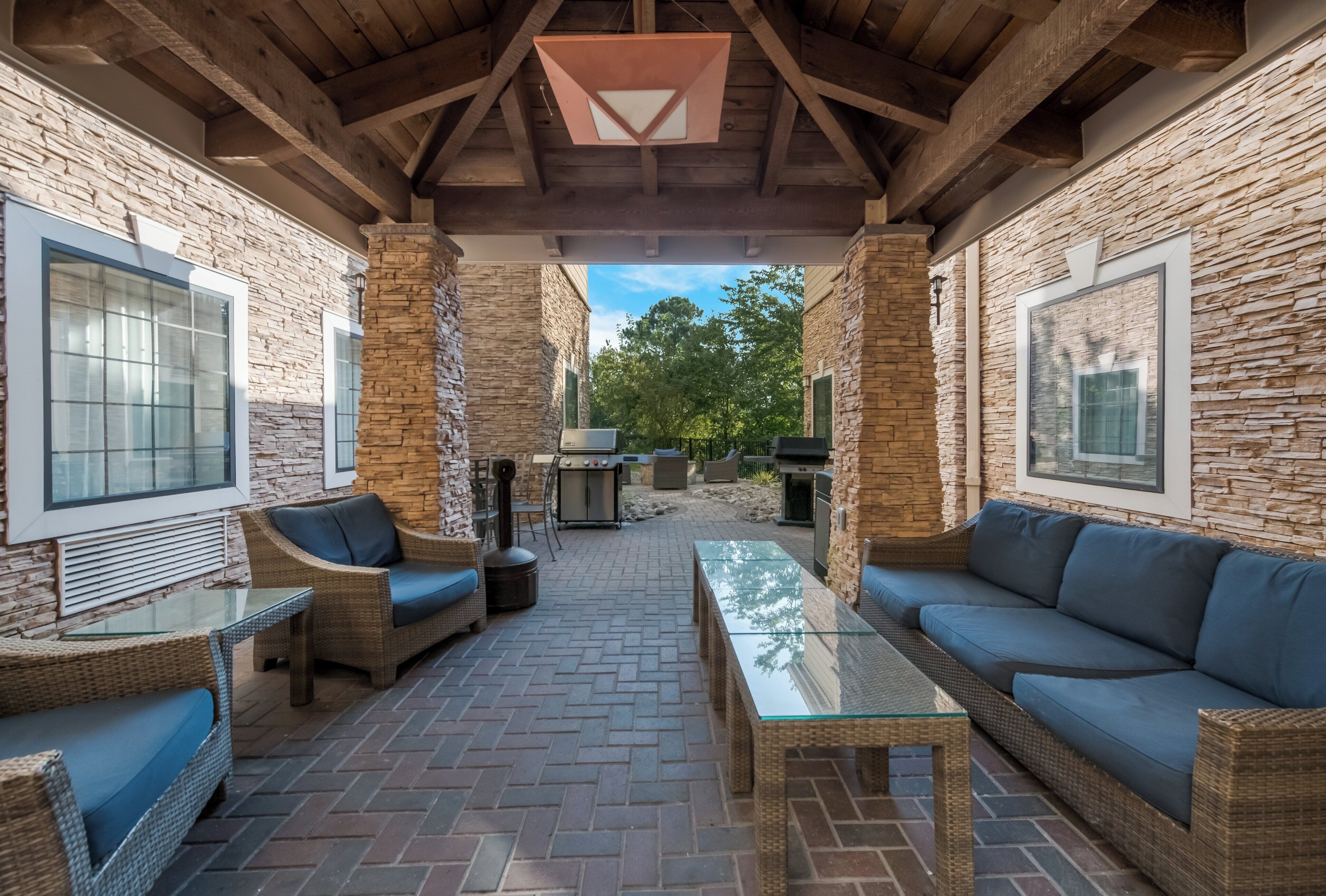 An outdoor patio with stone walls, wicker furniture, and a glass-top table.