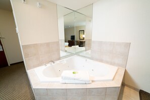 A modern bathroom with a large freestanding bathtub, a mirror, and a visible bed in the background.