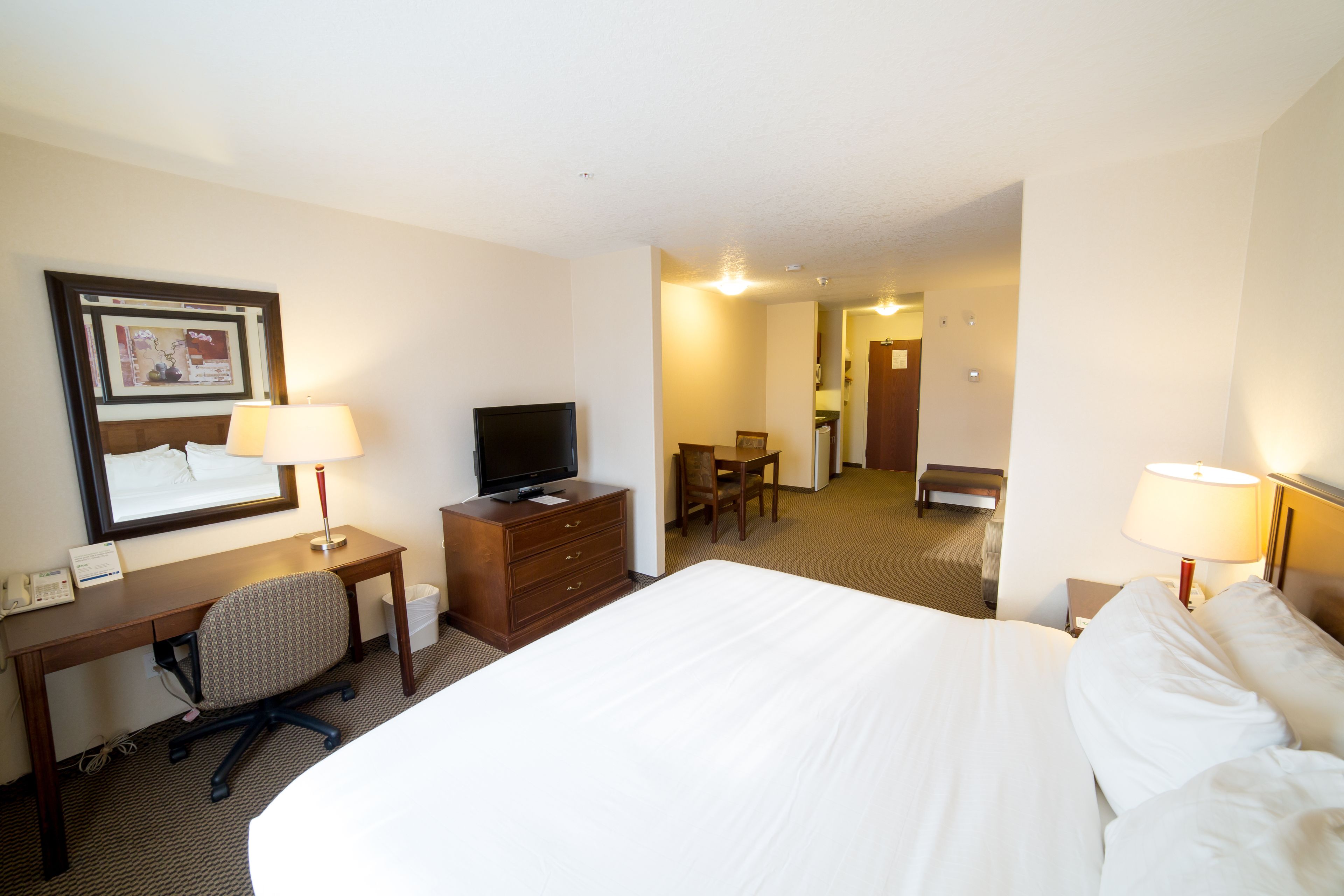 Habitación de hotel con una cama grande, un escritorio con silla, un televisor y una lámpara.