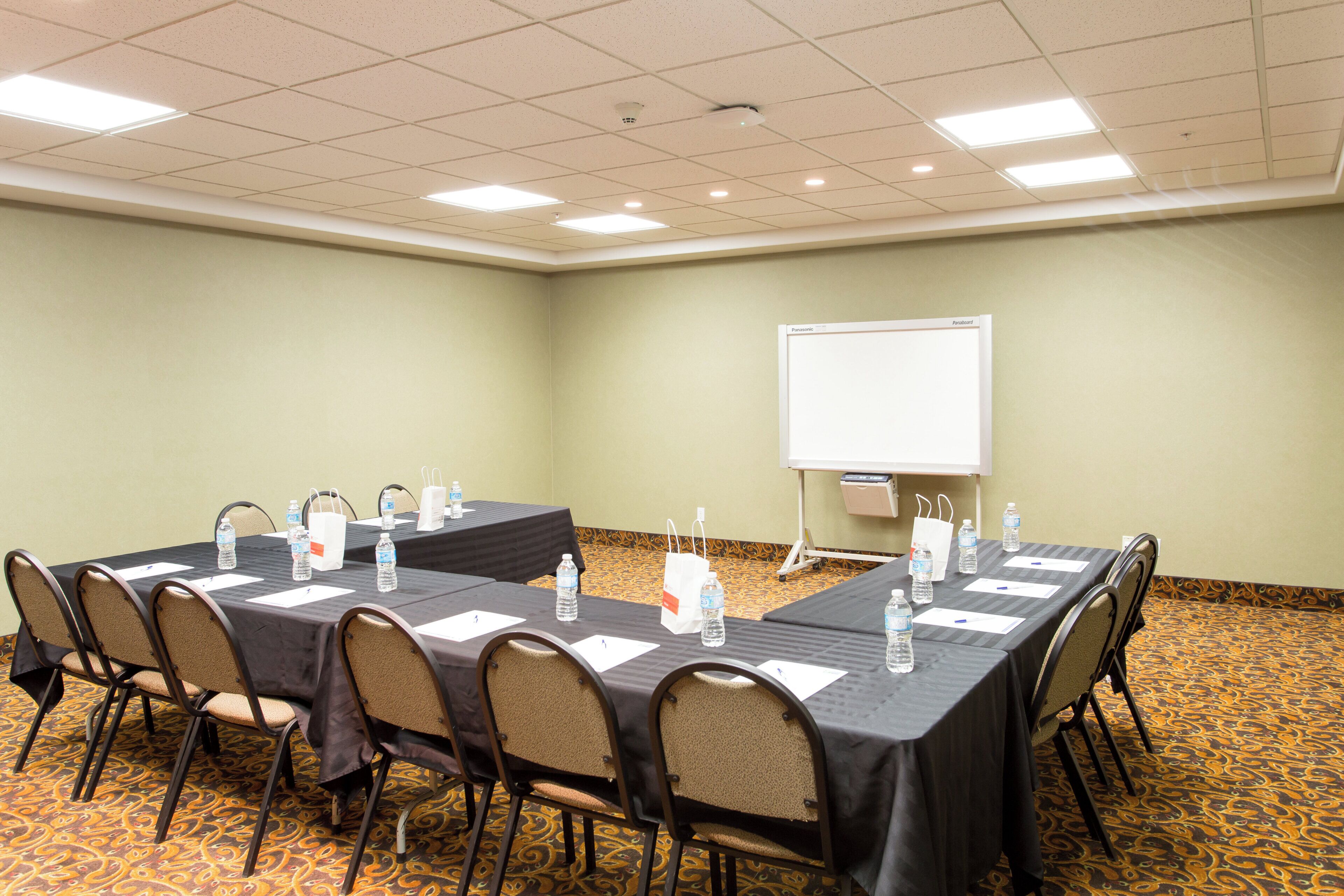 A conference room with a long table, chairs, water bottles, and a whiteboard.