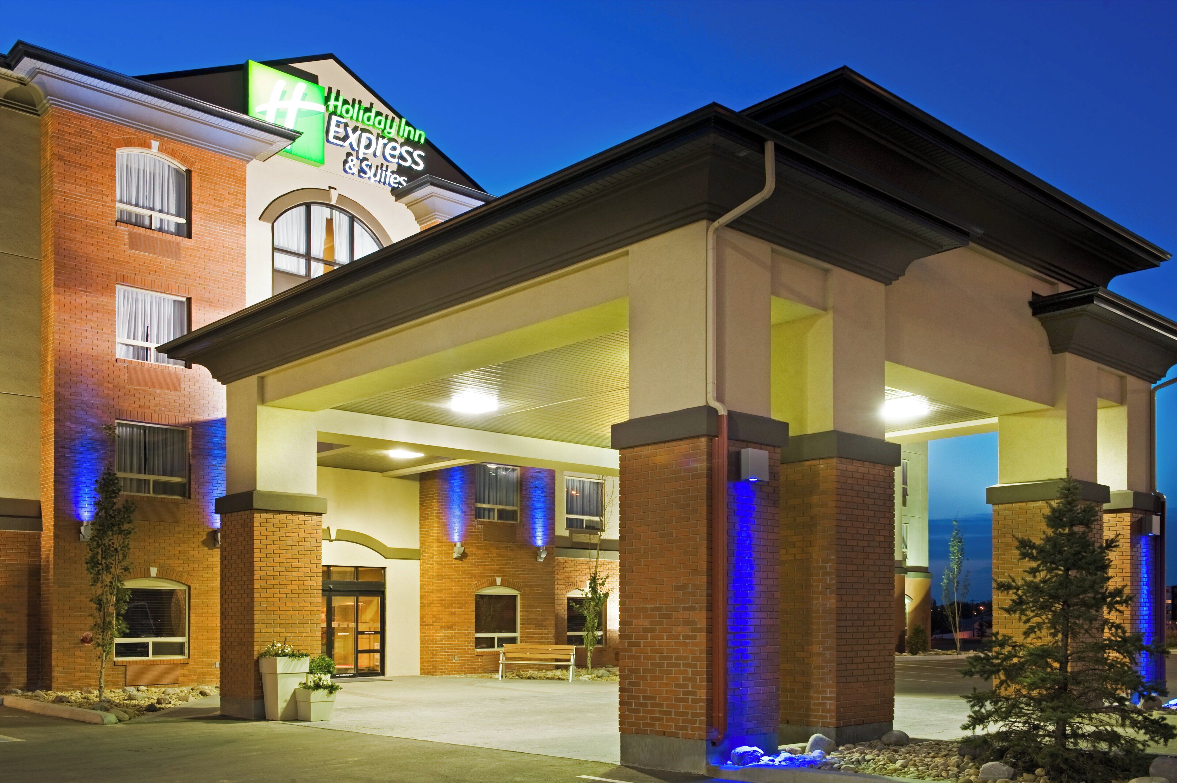A Holiday Inn Express & Suites building with a brick facade, large windows, and a covered entrance area.