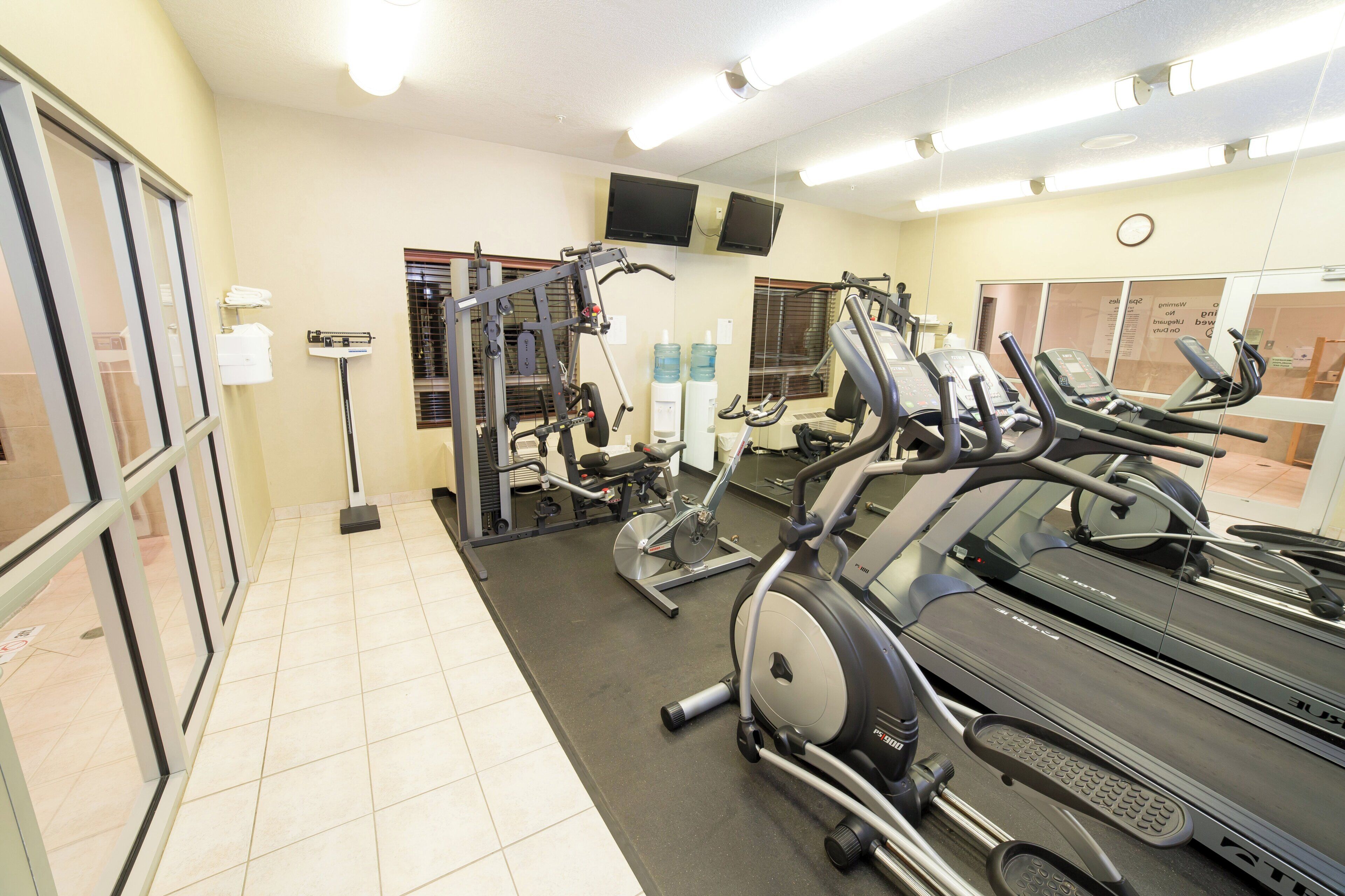 A gym with exercise equipment, including treadmills and weight machines, and a mirror on the wall.