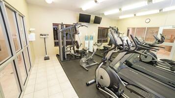 A gym with exercise equipment, including treadmills and weight machines, and a mirror on the wall.