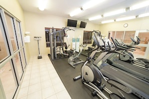 A gym with exercise equipment, including treadmills and weight machines, and a mirror on the wall.
