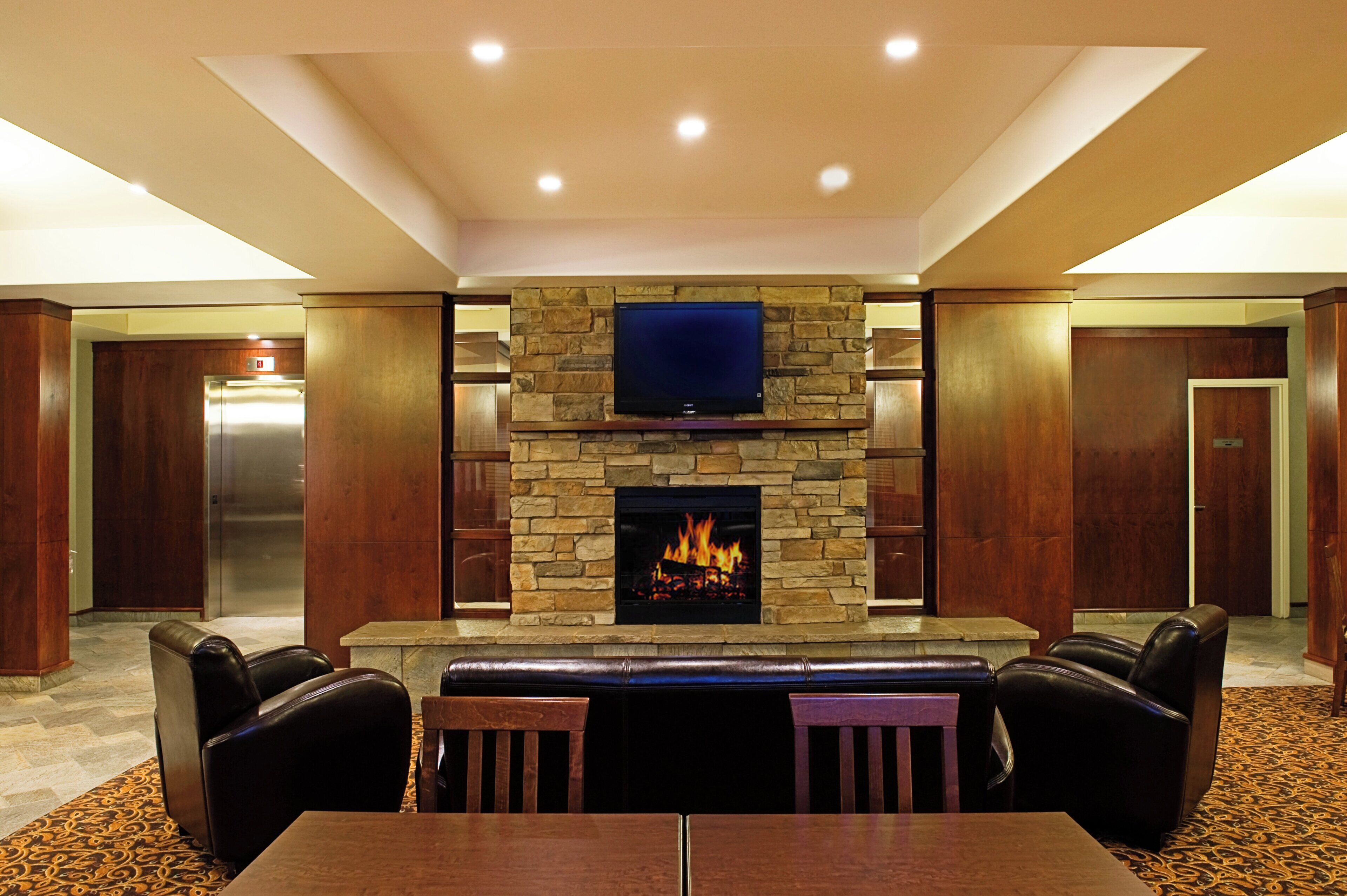 A hotel lobby with a stone fireplace, a flat-screen TV, leather seating, and a patterned carpet.