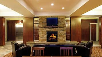 A hotel lobby with a stone fireplace, a flat-screen TV, leather seating, and a patterned carpet.