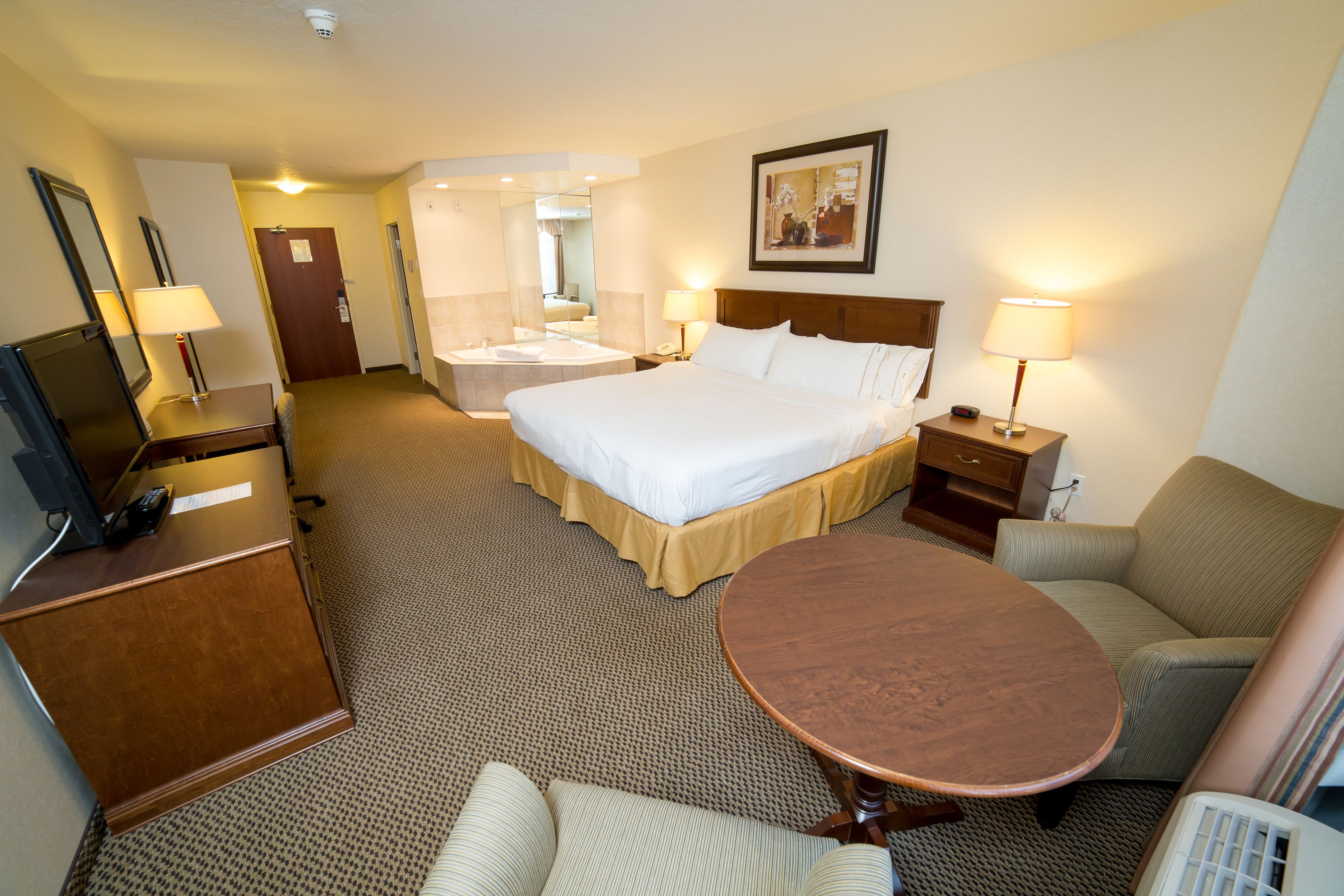 A hotel room with a bed, bedside table, lamp, chair, desk, and a small table.