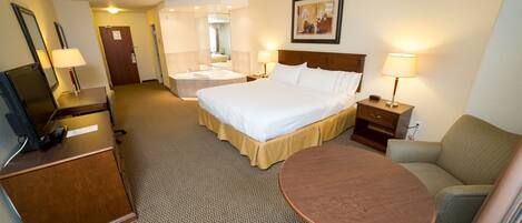 A hotel room with a bed, bedside table, lamp, chair, desk, and a small table.
