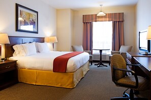 A hotel room with a large bed, two chairs, a desk, a lamp, a framed picture on the wall, and a window with curtains.