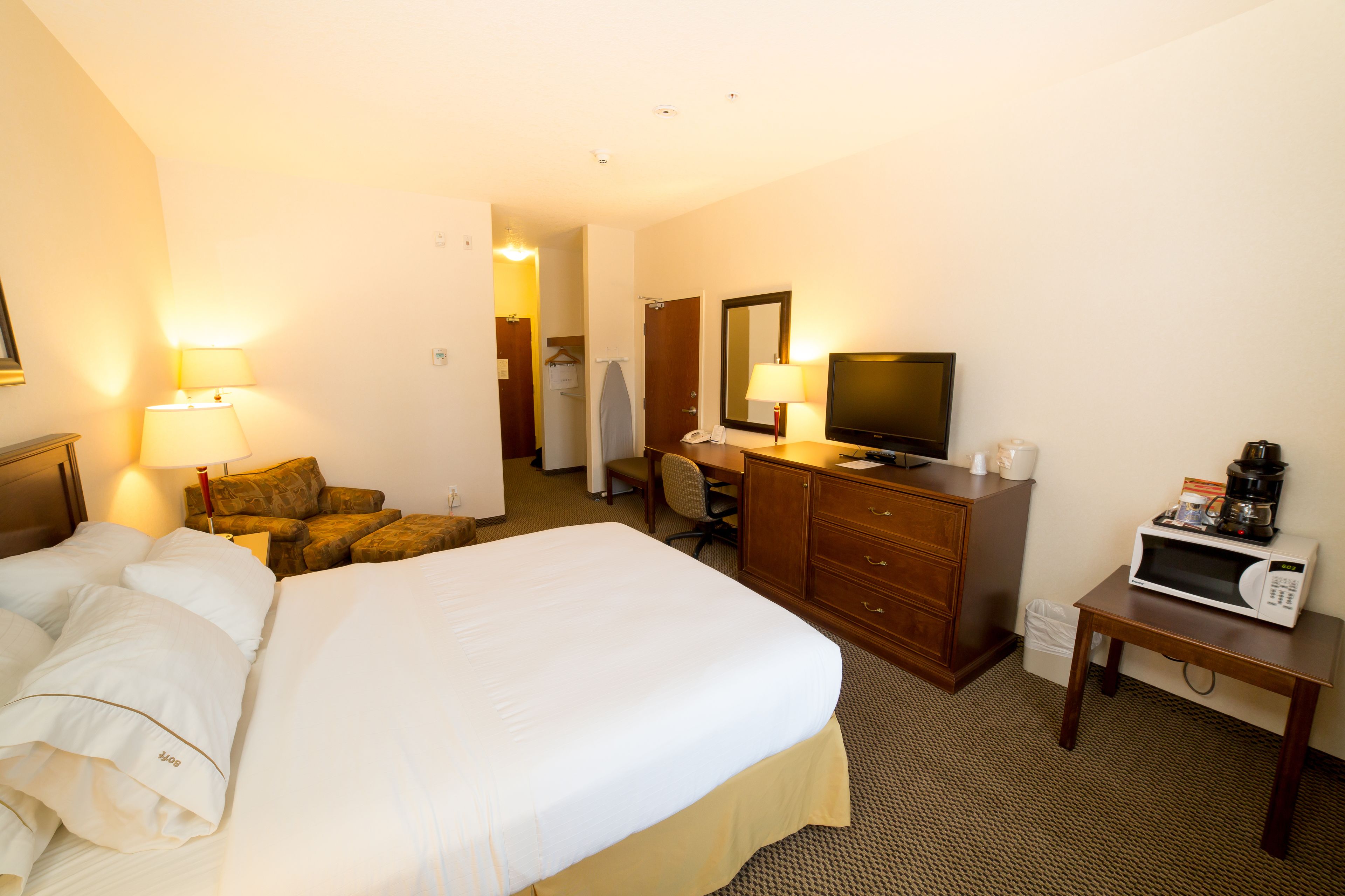 A hotel room with a large bed, a desk with a chair, a television, a microwave, and a small table.