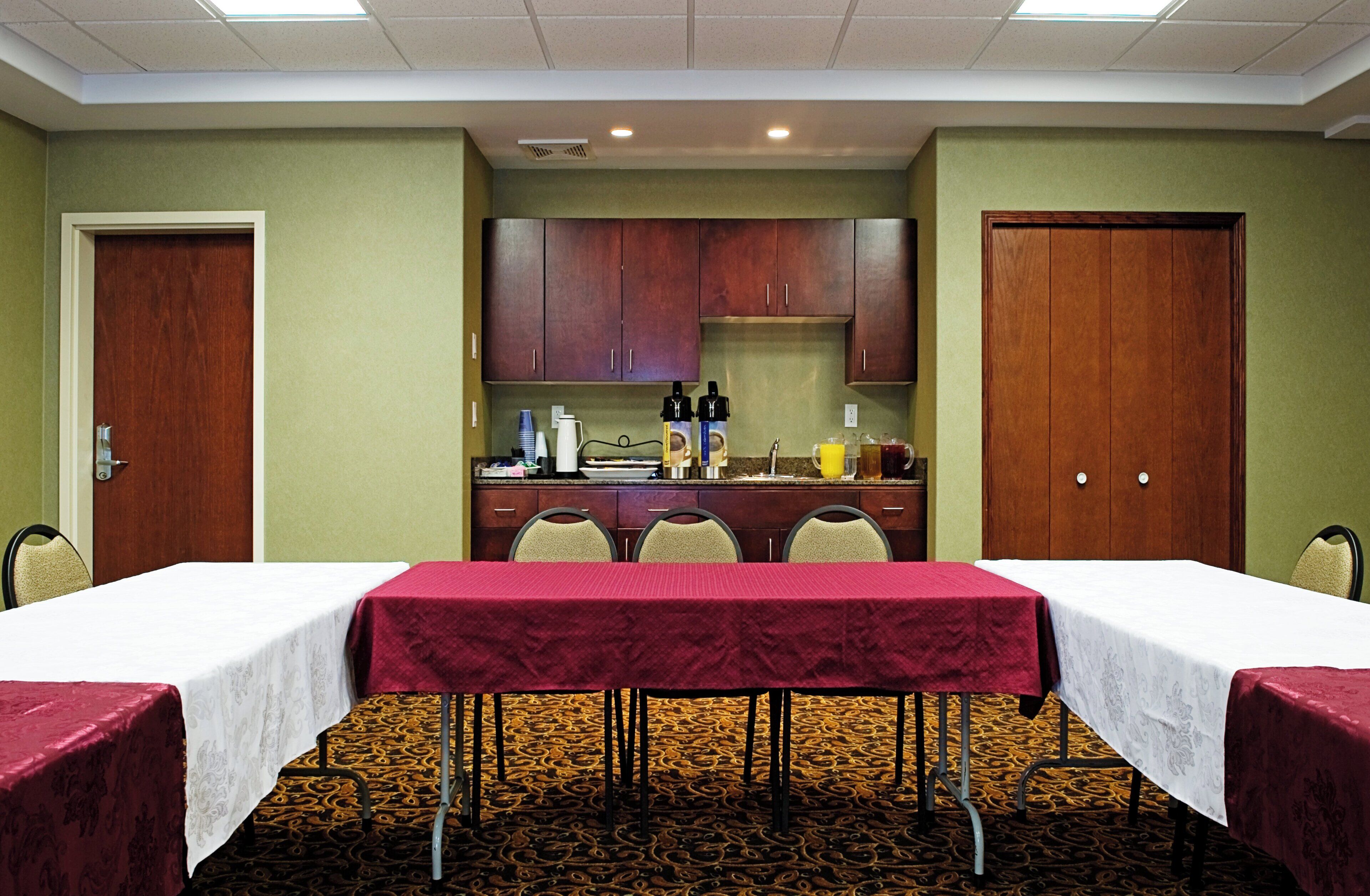 A conference room with two tables, chairs, a kitchenette, and a carpeted floor.