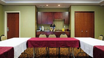A conference room with two tables, chairs, a kitchenette, and a carpeted floor.