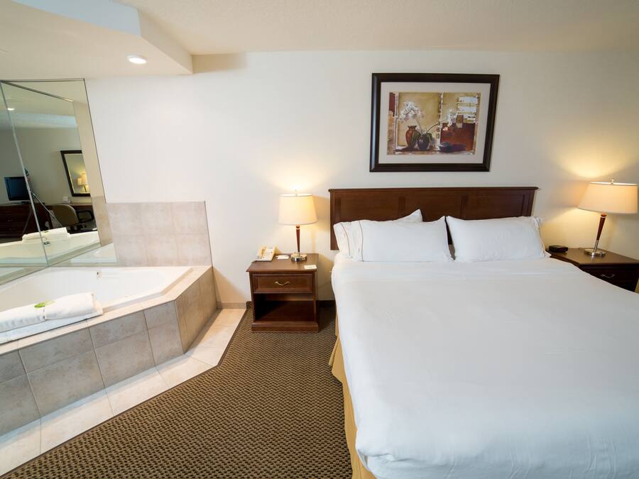 A hotel room with a large bed, a separate bathroom with a bathtub, a bedside table with a lamp, and a framed picture on the wall.