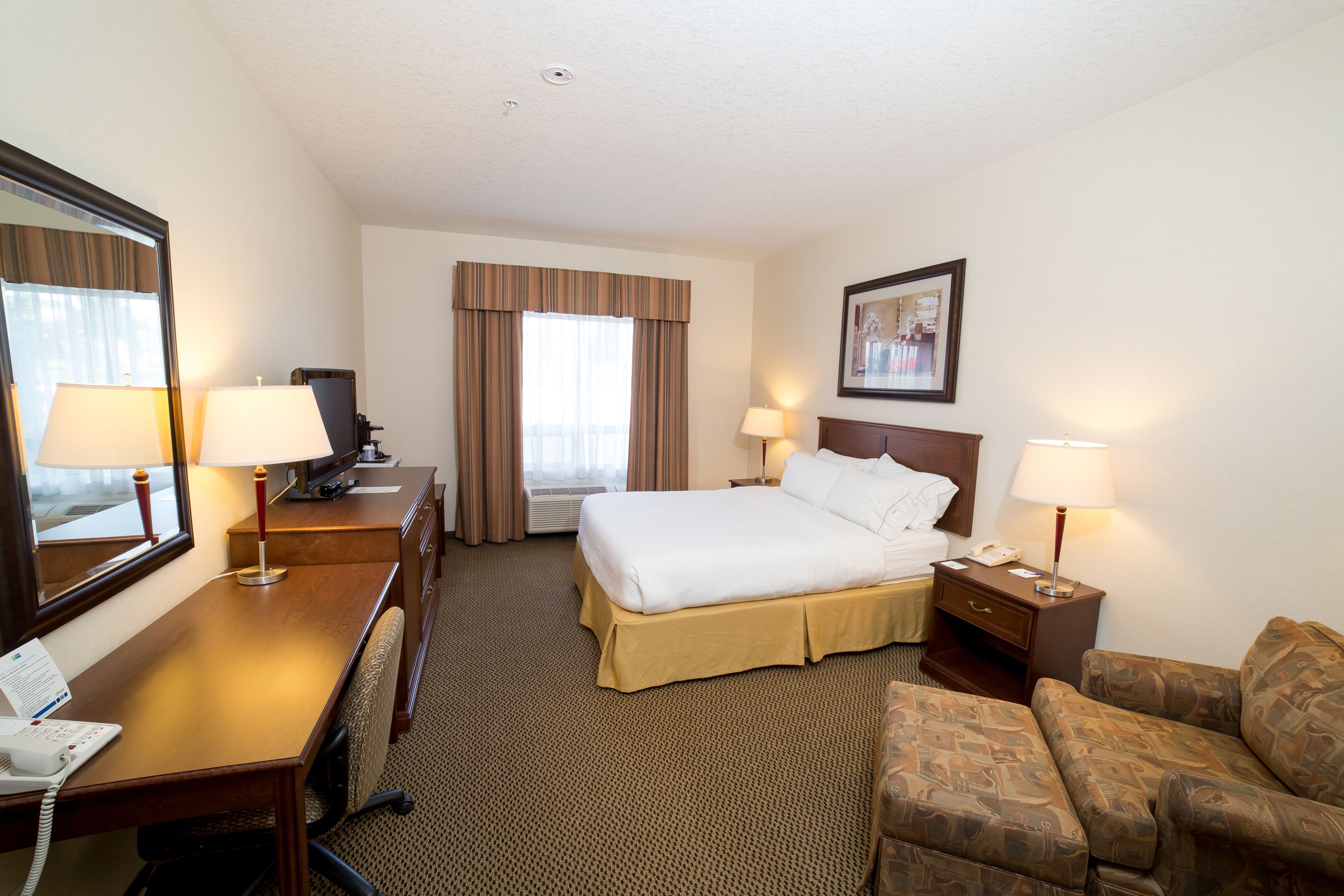 A hotel room with a bed, a desk with a telephone, a chair, a couch, and a window with curtains.