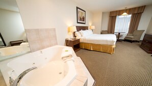 A hotel room with a large bathtub, a bed with white linens, a chair, a desk, and a window with curtains. - Holiday Inn Express Hotel & Suites Drayton Valley by IHG (Drayton Valley)