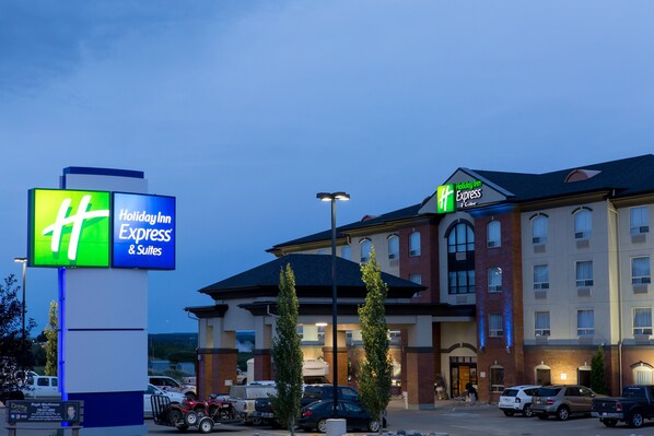 A Holiday Inn Express & Suites hotel with a large sign, parking lot, and a building with multiple windows and a brick facade.