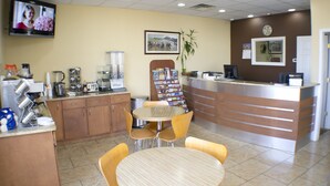 Un área de recepción con mostrador, máquina de café, televisor y una mesa con sillas.