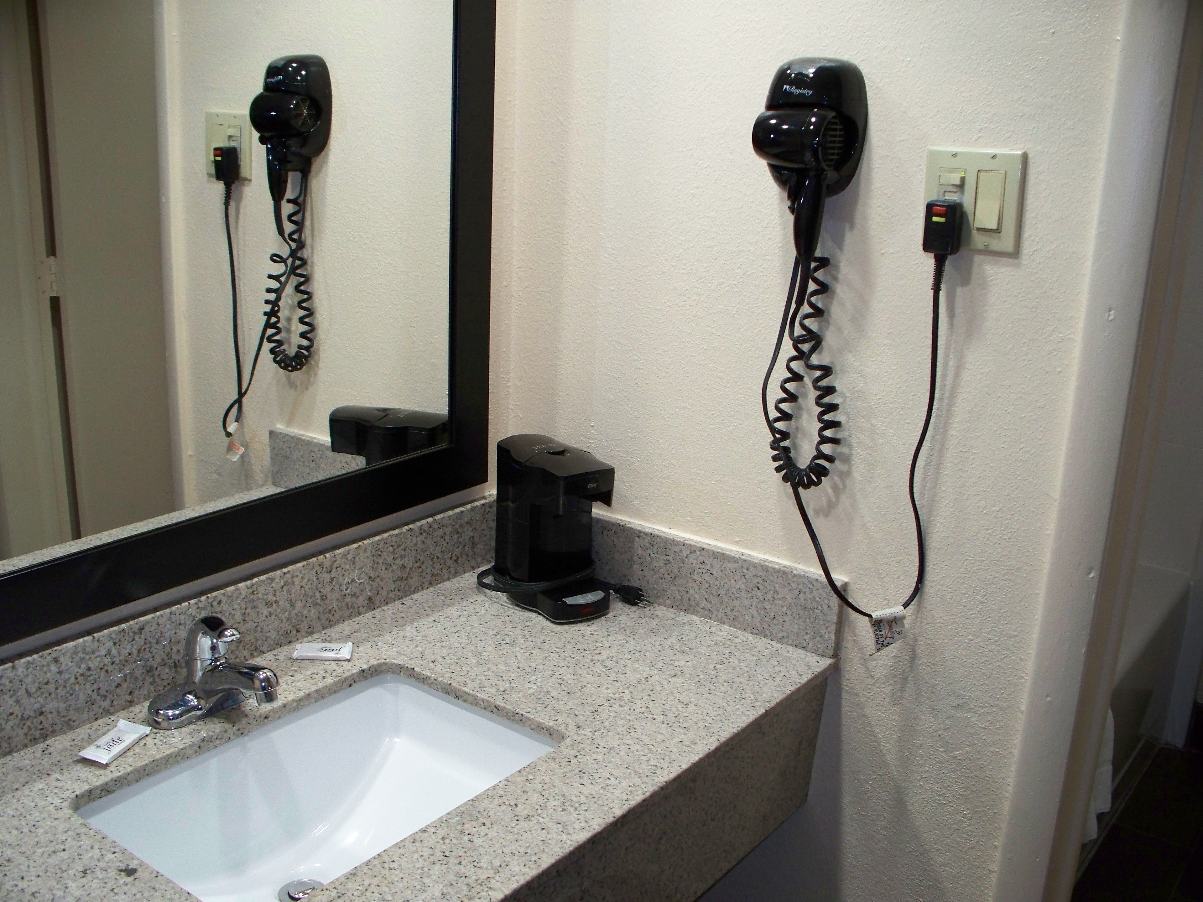 A bathroom with a sink, a mirror, a hairdryer, and a coffee maker.