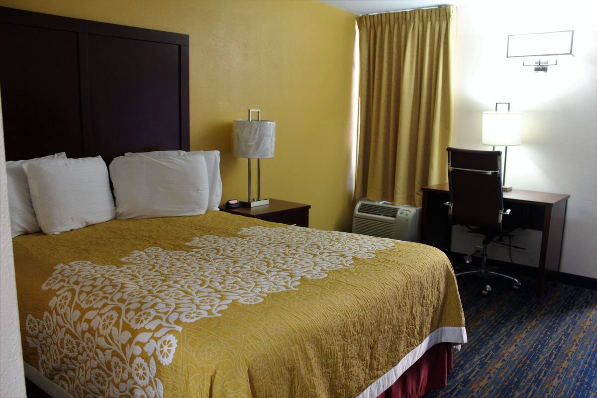 A hotel room with a large bed, a desk, a chair, a lamp, and a window with curtains.