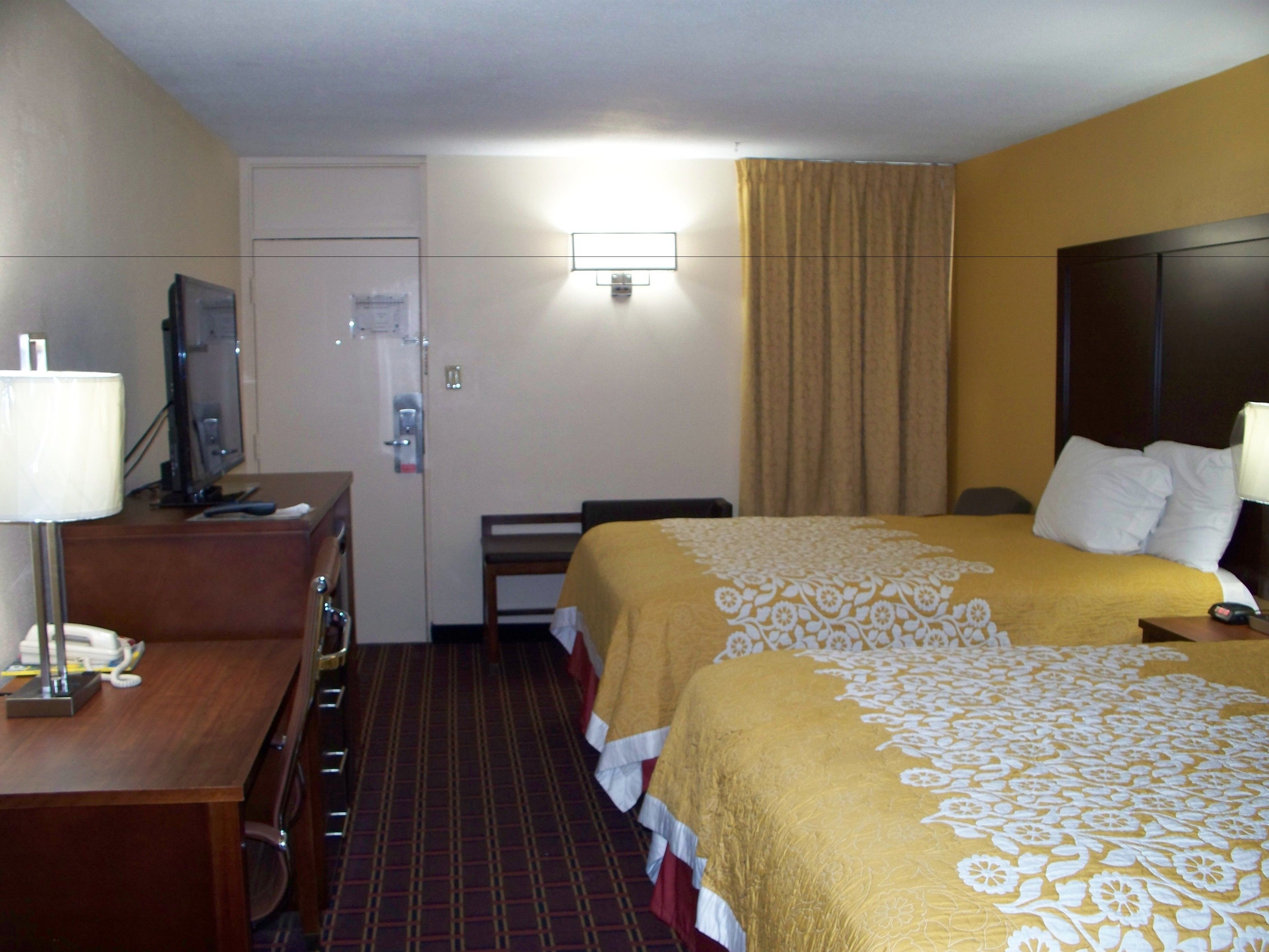 A hotel room with two beds, a desk with a television, a chair, and a bathroom door.